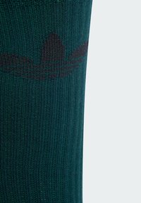 Calzino verde lavorato a maglia con texture a coste, caratterizzato da un motivo logo nero che somiglia a tre strisce di lato.