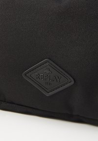 Black fabric bag featuring a textured surface and a diamond-shaped black rubber logo patch with "REPLAY" and "1981" embossed.