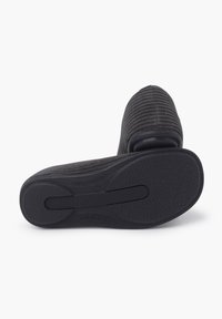 Scarpa nera slip-on con una tomaia in tessuto rigato e una suola in gomma testurizzata. La suola ha un design aerodinamico con una scanalatura centrale.