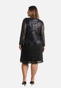 Černé flitrové šaty s dlouhými rukávy, přiléhavého střihu, ke kolenům. Texturované lesklými flitry; průsvitné prvky na rukávech a lemu.