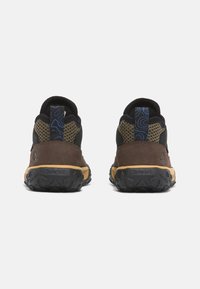 Hnědé a černé nízké boty s síťovými panely, texturovanou gumovou podrážkou a modrým vzorovaným akcentem na patě a na poutku.