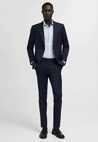 Temno modro suknjo s slim fit obliko, v kombinaciji s svetlo modro srajco. Črne usnjene čevlje dopolnjujejo formalni videz. Gladko, strukturirano blago.