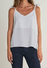 Top bianco senza maniche con sottili righe verticali blu navy, scollo a V e lacci alle spalline. Tessuto morbido con una vestibilità fluida e rilassata.