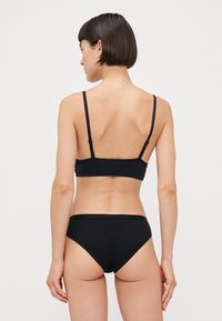 Black bikini set featuring a simple bralette with thin straps and matching high-waisted briefs. Smooth fabric with a fitted design.