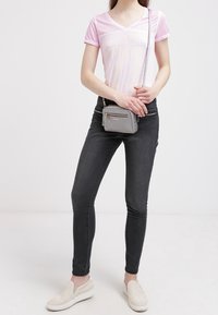 Ljusrosa v-halsad t-shirt med texturerade detaljer, i kombination med smala svarta jeans och en grå axelväska. Skorna är ljusbeiga slip-ons.