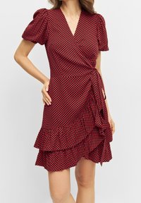 Robe rouge à manches courtes bouffantes, motif de cœurs dispersés, décolleté en V, ourlet volanté et détail de taille à nouer. Texture de tissu lisse.