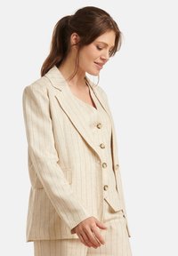 Beige gestreepte blazer met gelapte revers, met twee voorzakken en grote gouden knopen, gedragen over een bijpassend overhemd met knopen.
