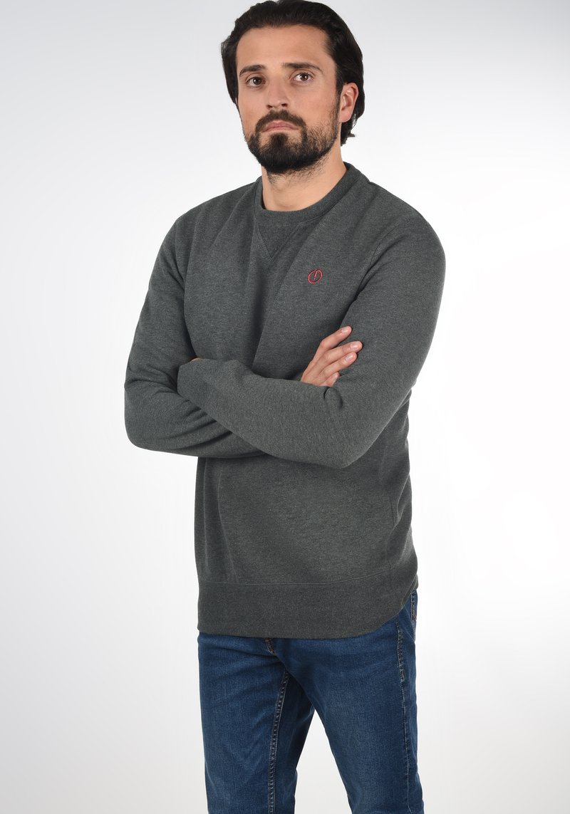 Grijze katoenen sweatshirt met ronde hals en geribde manchetten, voorzien van een klein rood logo op de borst. G gedragen met blauwe jeans.