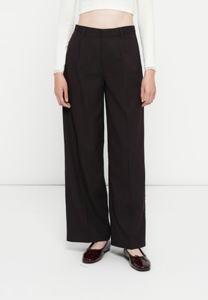 Bredde bukser i sort med striber, lavet af et glat materiale, med høj talje, skrædder-agtig design og sidelommer. Sammen med blanke sko.