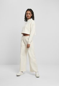 Lys beige cropped sweatshirt med høy krage, parret med høyt liv og vid bukse i matchende farge. Hvite sneakers fullfører antrekket.