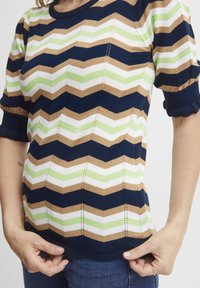 Pletený top s krátkým rukávem se zigzag vzorem v námořnické modré, béžové, bílé a světle zelené barvě. Obsahuje strukturovanou tkaninu a žebrované okraje.