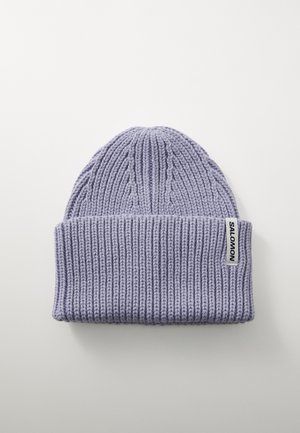 Purple knitted beanie with textured ribbing, featuring a fold-over cuff and a rectangular white label with black text on the side.