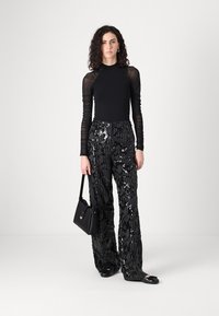 Top nero a maniche lunghe con maniche trasparenti e testurizzate, abbinato a pantaloni neri con paillettes dotati di un motivo verticale. Completano l'outfit una piccola borsa nera.