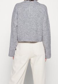 Szary, krótki sweter z ribbowym wykończeniem, długimi rękawami i miękką dzianiną. W zestawie z spodniami o podwyższonym stanie w kolorze ecru, z tylnymi kieszeniami.