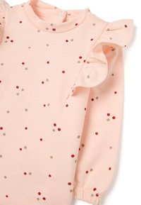 Top de manga larga rosa claro con hombros con volantes y lunares multicolores en rojo y beige, hecho de una tela suave.