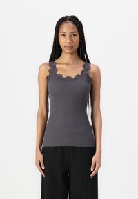 Top in cotone grigio a costine con pizzo sul collo e sulle spalline, dalla forma aderente e texture morbida. Indossato con pantaloni neri larghi.