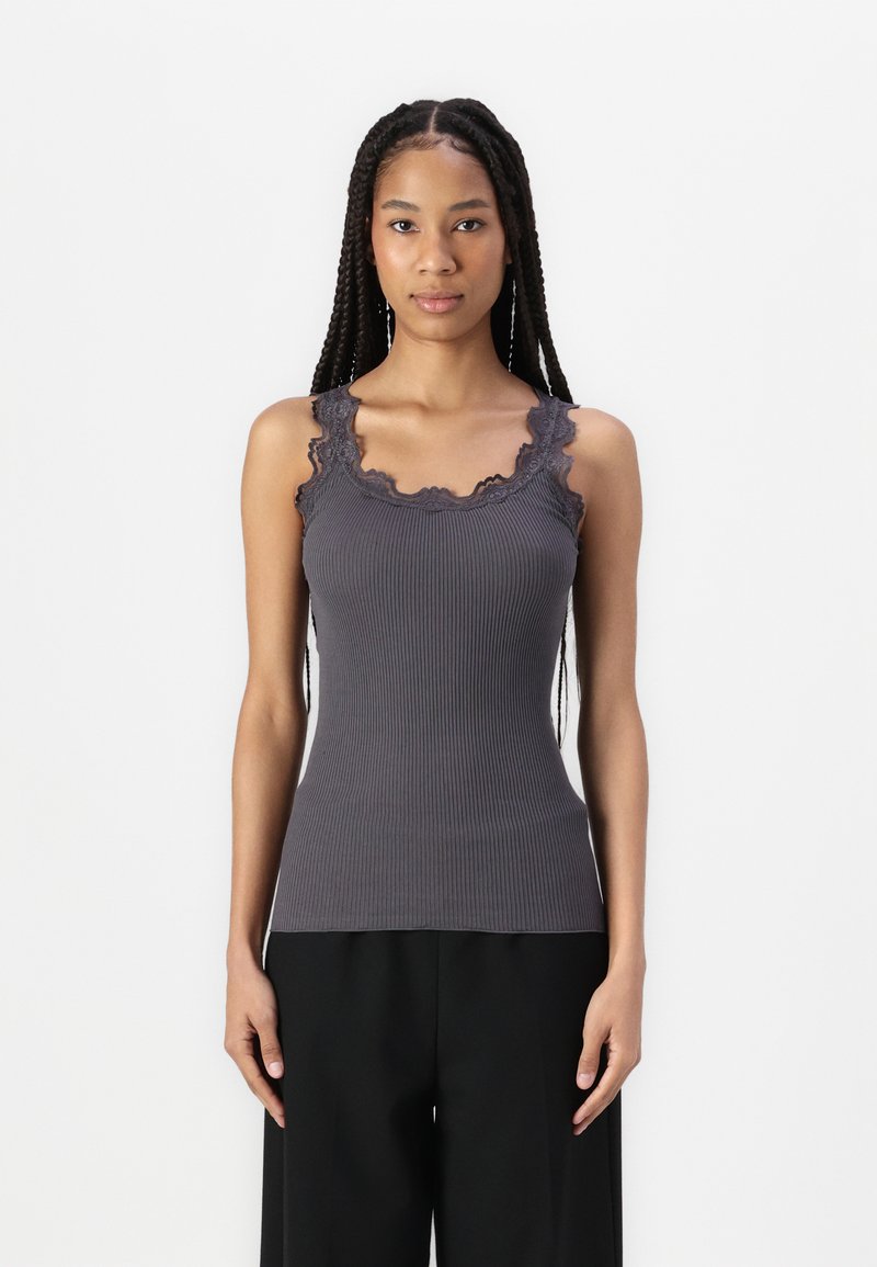 Top in cotone grigio a costine con pizzo sul collo e sulle spalline, dalla forma aderente e texture morbida. Indossato con pantaloni neri larghi.