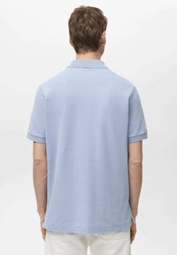 Vaaleansininen polo-paita, jossa on lyhyet hihat ja ribbireunus, valmistettu teksturoidusta kankaasta. Paita on suorahelmainen ja siinä on sivuhalkiot.