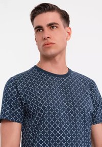 Námorně modré tričko s krátkým rukávem, které má opakující se bílé geometrické vzory, kulatý výstřih a měkkou bavlněnou texturu.