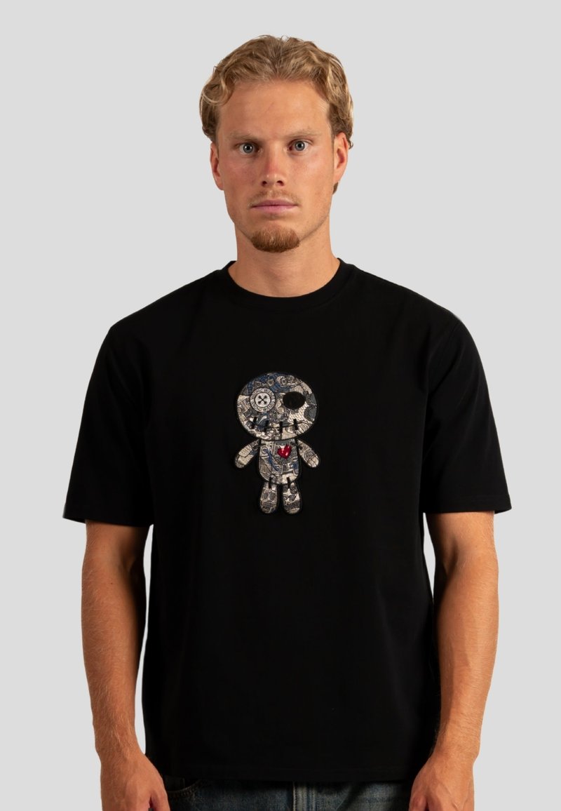 Černé bavlněné tričko s vyšitým barevným designem postavy, obsahující složité vzory a červené srdce umístěné uprostřed.
