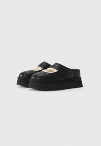 Sorte slip-on platform sko med runde tæer og beige fuzzy foring synlig rundt om åbningen, på en ensfarvet hvid baggrund.