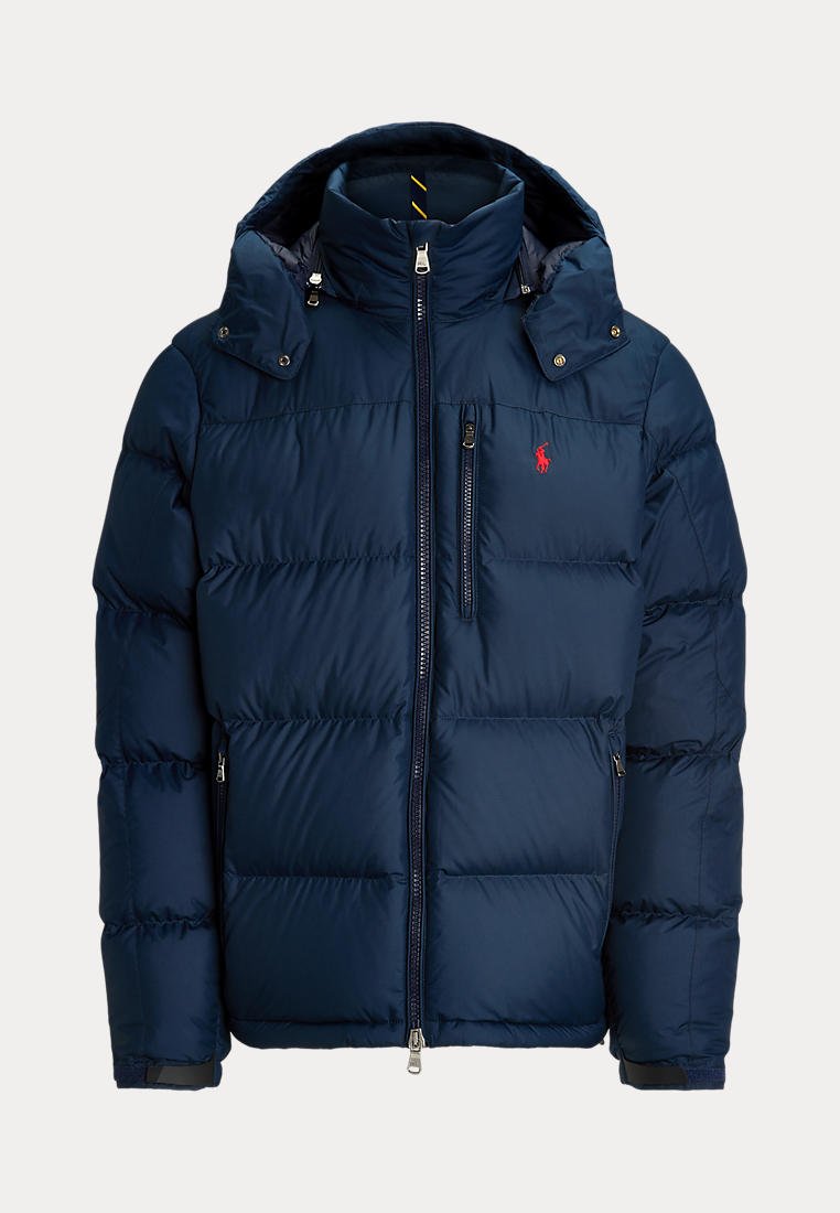 Doudoune bleu marine avec col montant, capuche amovible, poches zippées à l'avant et sur la poitrine, et logo rouge brodé sur la poitrine.