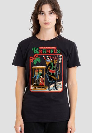 Woman wearing black t-shirt showing Krampus with children in a cage on a sled, holding chains and a skull staff, with festive holly decoration.