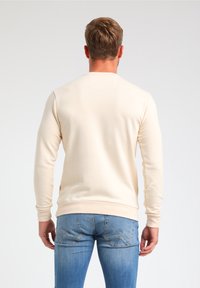 Sudadera de color beige claro con mangas largas, puños y dobladillo acanalados. Fabricada con un material suave, presenta un sutil detalle de logo en el lateral.