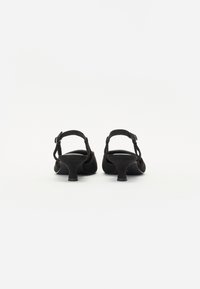 Sandalias de tacón alto de ante negro con punta redonda, correa en el tobillo y un tacón bajo y grueso. Diseño minimalista y textura suave.