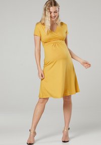 Gelbes, kurzärmliges Wickelkleid mit tailliertem Oberteil und ausgestellt Rock, aus weichem Stoff gefertigt, mit einem gerafften Detail unter der Brust.
