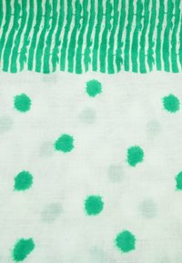 Katoenen stof met een witte achtergrond heeft groene strepen aan de bovenkant en verspreide groene stippen in verschillende tinten overal.