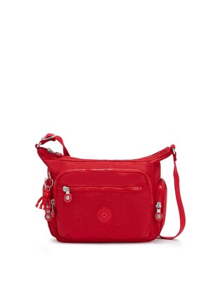 Sac bandoulière rouge avec plusieurs poches zippées, bandoulière réglable et une petite figurine porte-clés attachée à un côté.