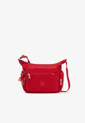 Sac bandoulière rouge avec plusieurs poches zippées, bandoulière réglable et une petite figurine porte-clés attachée à un côté.