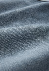 Helehall sinine teksakangas, millel on tekstuuriga sooniline kudumine, peened diagonaalsed jooned ja pehme, mõnevõrra läikiv pind.