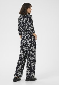 Jumpsuit floral con fondo azul marino oscuro, que presenta flores blancas y grises; corte relajado con cintura ajustable y mangas de tres cuartos.