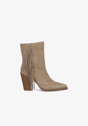 Beżowe zamszowe botki za kostkę z szpiczastym noskiem, z ozdobnym frędzlem po boku i drewnianą, warstwową podeszwą. Gładka tekstura i minimalne przeszycia.