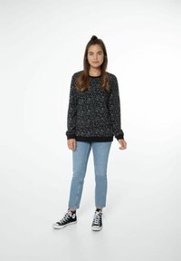 Felpa nera a fantasia con maniche lunghe e polsini a costine, abbinata a jeans azzurri chiari e sneakers alte nere.