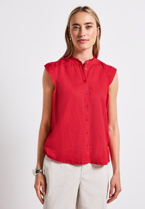 Blouse rouge à manches courtes avec col mandarin, fermeture à boutons sur le devant et tissu doux et texturé. Coupe décontractée avec un léger drapé.