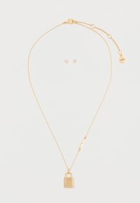 Collana in tono oro con pendente a forma di lucchetto e incisione "DKNY", abbinata a orecchini a perno coordinati con pietre trasparenti.