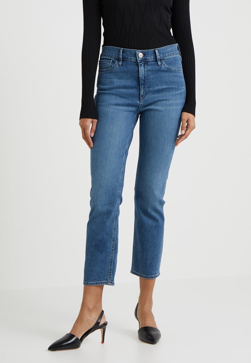 Blå denimjeans med midjepassform, rak ben och beskuren fåll. Har fem fickor och en ljus tvätt. Bärs med svarta slingbacks.