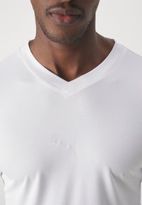 T-shirt de sport blanc texturé avec un col en V et un motif en grille subtil, arborant un logo Puma blanc réfléchissant sur la poitrine.