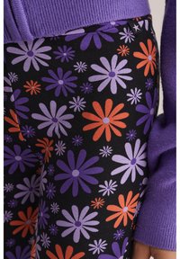 Leggings noirs avec un motif floral comprenant des fleurs violettes, oranges et blanches. Fabriqués en tissu doux et extensible avec une coupe ajustée.
