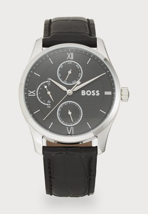 Montre avec bracelet en cuir noir, boîtier en acier inoxydable argenté, cadran texturé noir, chiffres romains proéminents et trois sous-cadrans pour la date et l'heure.