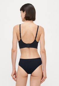 Melns krūšturis ar regulējamiem siksnām un aizdari, precīzi apvienots ar atbilstošām melnām augsto vidukļa biksītēm. Gluda auduma ar minimālistisku dizainu.