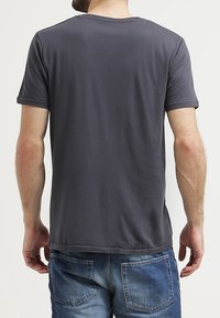 Šedé tričko s krátkým rukávem, kulatým výstřihem a hladkou strukturou, v kombinaci s modrými džínami s zadními kapsami.