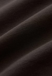 Tejido marrón oscuro suave y elástico con una textura de fina acanaladura, que muestra pliegues sutiles y tonos variados debido a la iluminación.
