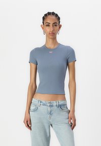 Gray ribbed short-sleeve top with a fitted design and a small red logo on the chest, paired with light blue denim jeans.