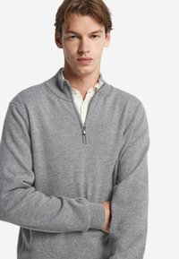 Ljusgrå zip-up tröja i mjukt material, med hög krage, långa ärmar och ribbade muddar. Slät textur och enkelt design.