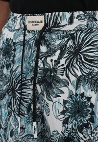 Shorts da bagno floreali bianchi con motivi turchesi e neri. Presentano una vita elastica, un laccetto e l'etichetta Just Cavalli.
