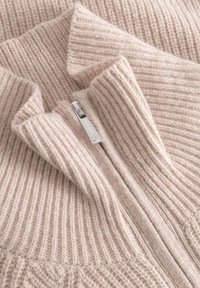 Helles rosa Strickpullover mit geripptem Muster, hohem Kragen und silbernem Reißverschluss. Weiches Material mit einem gemütlichen Erscheinungsbild.